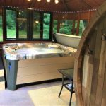 Indoor hot tub with a windowed view, wooden seating area, plants, and hooks on a paneled wall in a cozy room.