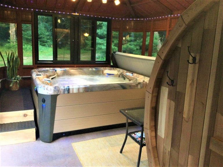 Indoor hot tub with a windowed view, wooden seating area, plants, and hooks on a paneled wall in a cozy room.