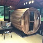 Wooden barrel sauna in a cozy room with a sofa, colorful pillows, and small table.