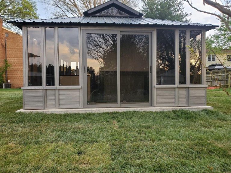 Outdoor wooden shed with glass sliding doors and corrugated roof, surrounded by grass and trees.