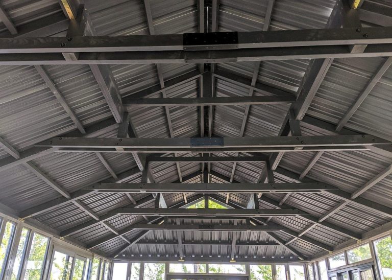 Interior view of a pitched metal roof with exposed beams and windows below.